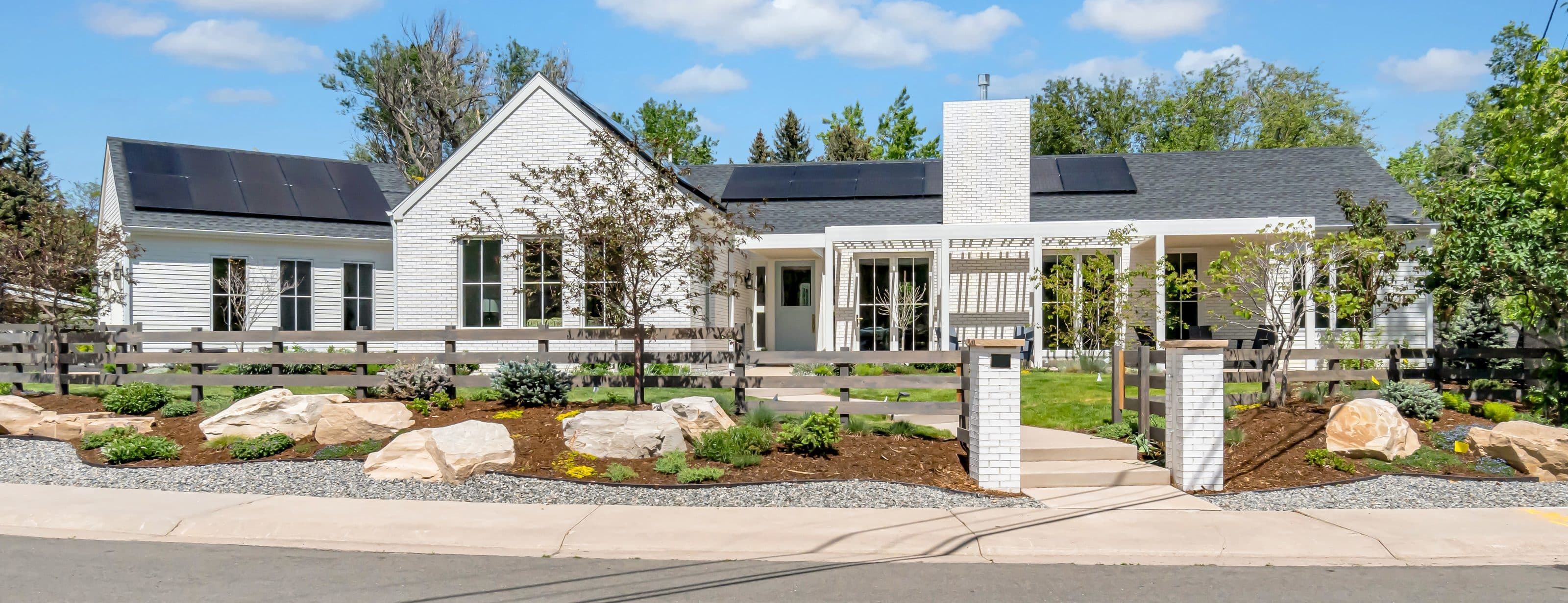 A white Boulder farmhouse with a deep front porch behind a split-rail fence